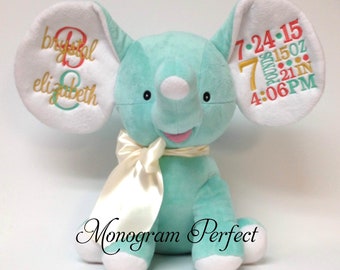 May include: A plush turquoise elephant with white ear linings and a cream-colored ribbon. The elephant's ears are embroidered with names and birth details. The text "Monogram Perfect" is at the bottom.