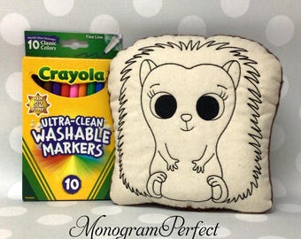 May include: A plush hedgehog pillow with black outline details and large black eyes. Next to it is a box of Crayola Ultra-Clean Washable Markers, 10 classic colors. The text "Monogram Perfect" is at the bottom.