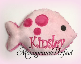 May include: Pink plush fish with pink polka dots and the name "Kinsley" embroidered on it. The fish is a personalized gift for a child.
