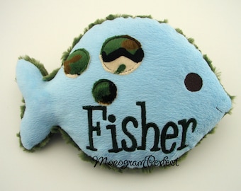May include: A light blue plush fish with a camouflage pattern and the name "Fisher" embroidered on it.