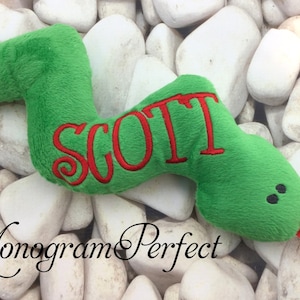 May include: Green plush snake toy with a red embroidered name "SCOTT" on the side. The snake has black eyes and a red tongue.