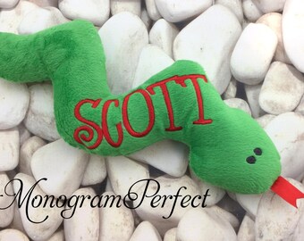 May include: Green plush snake toy with a red embroidered name "SCOTT" on the side. The snake has black eyes and a red tongue.