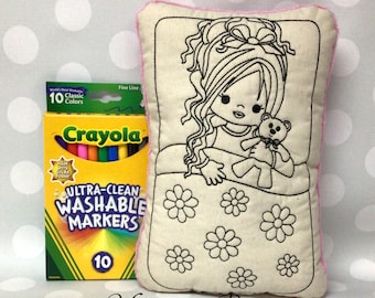 May include: A coloring pillow with a girl and teddy bear design, next to a box of Crayola Ultra-Clean Washable Markers. The pillow has a pink border and the text "Monogram Perfect" at the bottom.