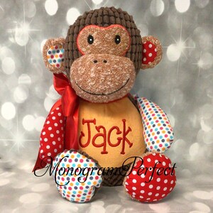 May include: A brown plush monkey toy with red, white, and blue polka dot fabric on its arms and legs. The monkey has a red ribbon around its neck and a tan patch on its chest with the name "Jack" embroidered in red thread.