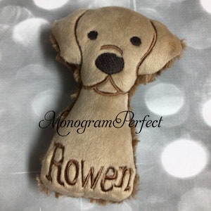 Könnte beinhalten: Ein Plüschtier in Form eines braunen Hundes mit gestickten Augen, Nase und Mund. Das Spielzeug ist mit dem Namen "Rowen" in brauner Stickerei personalisiert.