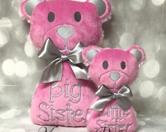 May include: Two pink plush teddy bears with silver bows and embroidered text. The larger bear says "Big Sister" and the smaller bear says "Little Sister".