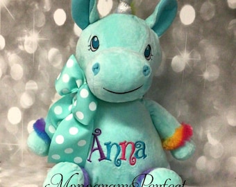 May include: A turquoise plush unicorn with a silver horn, rainbow trim, and a white polka dot bow. The unicorn is embroidered with the name "Anna" and the words "Monogram Perfect".