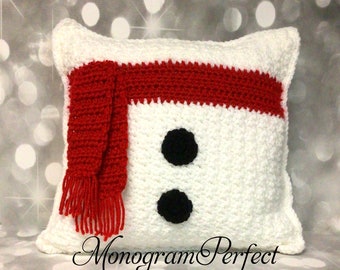 May include: White crocheted pillow with a red scarf and black button eyes. The pillow has the text "Monogram Perfect" at the bottom.