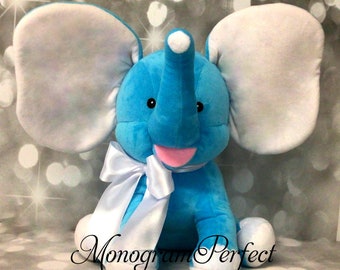 May include: A plush blue elephant toy with white ears and a white bow. The elephant has a pink tongue sticking out and black eyes.