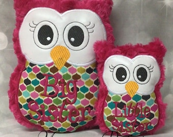 May include: Two plush owl-shaped pillows. The larger owl has "Big Sister" embroidered on its front, and the smaller owl has "Little Sister." Both owls are pink with white faces, large eyes, and patterned fabric on their chests. The text "Monogram Perfect" is at the bottom.