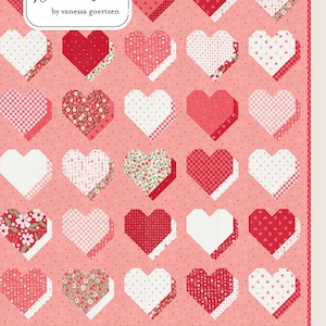 May include: A quilt with a pattern of red and white hearts on a pink background. The hearts have various designs, including polka dots, floral prints, and solid colors. The quilt is labeled "Beloved" and "Lella Boutique by vanessa goertzen."