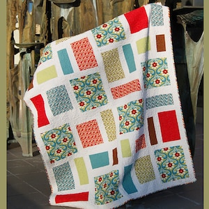 May include: A Pepperland quilt with a white background and colorful rectangular patterns. The quilt features red, blue, yellow, and brown blocks with floral and patterned designs. The quilt is from Abbey Lane Quilts.