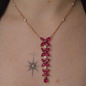 May include: A rose gold chain necklace featuring a vertical pendant composed of four flower-shaped clusters of marquise-cut deep pink gemstones, interspersed with small round clear stones, ending in a single pear-cut deep pink gemstone drop.