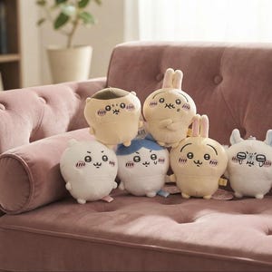 May include: A collection of six small, round plush toys featuring various cartoon characters with embroidered facial expressions, including blushing cheeks and simple line-drawn eyes and mouths, arranged in a group on a tufted sofa.