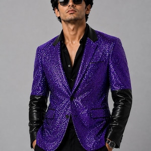 Puede incluir: Un blazer de lentejuelas en color morado vibrante con mangas de cuero negro en contraste y solapa negra. La chaqueta se lleva sobre una camisa negra abotonada y se combina con pantalones negros. La prenda incluye dos bolsillos y dos botones.