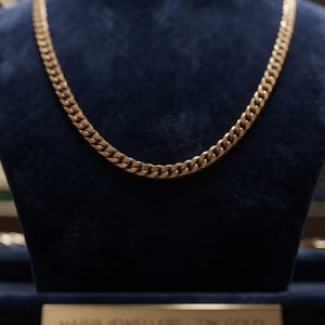 Puede incluir: Un collar de cadena dorada con eslabones entrelazados en un estilo de cadena barbada clásico. El metal tiene un acabado pulido que refleja la luz. Una pequeña placa rectangular en la base muestra el texto HABIB JEWELLERS - 22K GOLD.