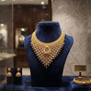 Puede incluir: Un collar de oro con un intrincado patrón de filigrana y cuentas colgantes, junto con pendientes jhumka a juego en forma de campana y un brazalete de oro texturizado. El conjunto presenta un trabajo de metal detallado y acabado dorado.