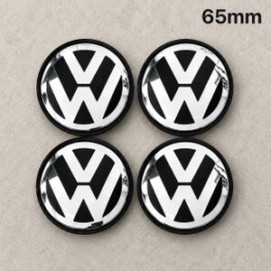 Può includere: Un set di quattro coprimozzo circolari, ciascuno con il logo Volkswagen nero e argento e un diametro di 65mm. I tappi hanno una finitura lucida con un anello esterno nero e un emblema centrale che mostra le lettere VW in argento.