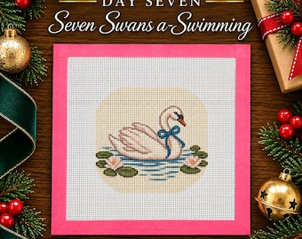 May include: A square needlepoint canvas featuring a white swan with a blue bow swimming on blue water with pink water lilies, framed by a bright pink border. The text reads DAY SEVEN Seven Swans a-Swimming in white and gold lettering.