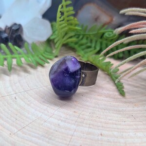 May include: A purple amethyst stone ring with a silver band. The ring is set on a wooden surface.