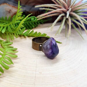 May include: A ring with a large, purple amethyst stone set in a brass band.