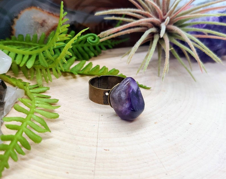 May include: A ring with a large, purple amethyst stone set in a brass band.