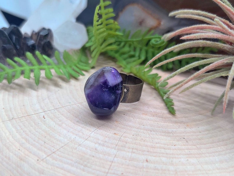 May include: A purple amethyst stone ring with a silver band. The ring is set on a wooden surface.