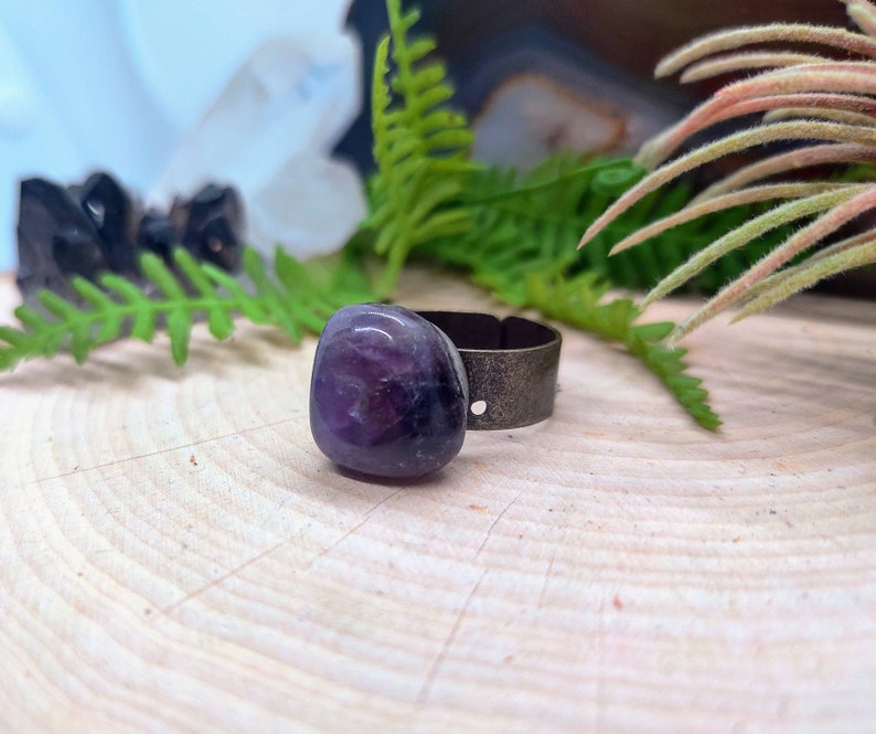 May include: A purple amethyst stone ring with a silver band. The ring is sitting on a wooden surface.