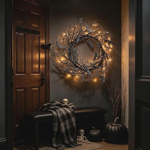 May include: A circular wreath made of dark, bare branches adorned with small warm-toned fairy lights and several small bat figures. The wreath is mounted on a dark wall above a black bench draped with a black and white plaid blanket.