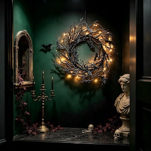May include: A circular wreath made of dark, twisted branches adorned with small, glowing warm white fairy lights and several black bat silhouettes. The wreath is mounted on a dark green wall, accompanied by a gold candelabra and a stone bust.