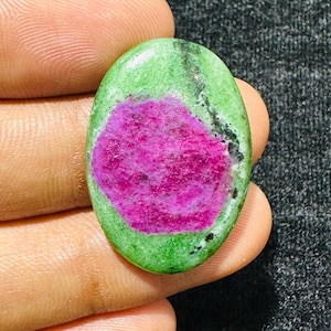 Può includere: Una pietra preziosa lucidata di forma ovale caratterizzata da un vivace centro rosa magenta circondato da un bordo screziato verde chiaro e verde scuro con inclusioni minerali nere su tutta la superficie della pietra, con una finitura liscia e lucida.