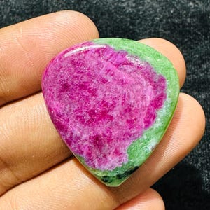 May include: A polished, teardrop-shaped zoisite gemstone featuring a vibrant, deep magenta-pink center surrounded by a contrasting border of mottled lime green and dark forest green mineral inclusions with a smooth, reflective surface texture.