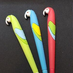 Könnte beinhalten: Drei Papageien-förmige Stifte, einer grün, einer blau und einer rot. Die Stifte haben ein 3D-Papageien-Design mit gelben, grünen und blauen Akzenten.