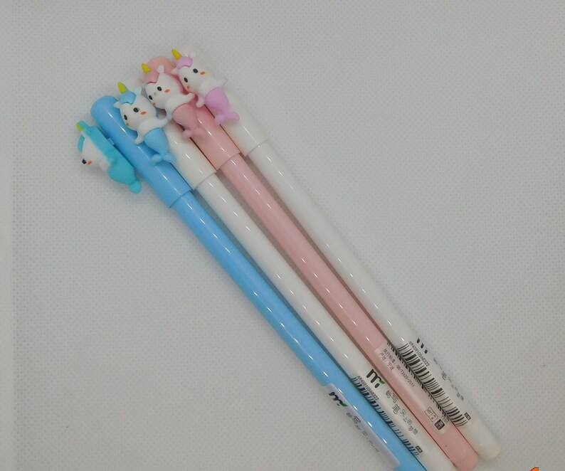 May include: Four unicorn-shaped pens with blue, pink, and white barrels. The pens have a unicorn head with a gold horn and a mermaid tail.