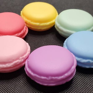 Pode incluir: Seis macarons de cor pastel dispostos em círculo sobre uma superfície preta. Os macarons são rosa, amarelo, verde claro, azul claro, roxo e rosa claro.