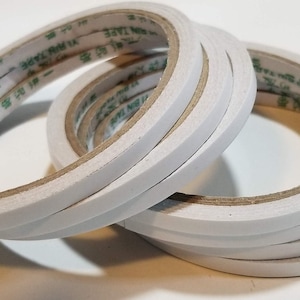 May include: A roll of white double-sided tape with a green label that reads "30MMX10M 1A".