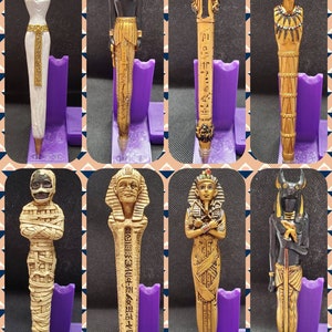 May include: Set of ten Egyptian themed pens, each featuring a different deity or symbol. The pens are made of resin and have a gold finish. The deities include Anubis, Bastet, Horus, Isis, Osiris, Ra, Sekhmet, Thoth, and the Eye of Horus. The pens are approximately 6 inches long.