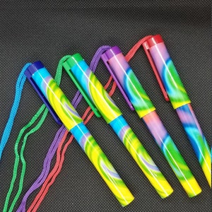Puede incluir: Cinco bolígrafos coloridos con un patrón de espiral y una cuerda atada a cada uno. Los bolígrafos están dispuestos en un patrón de arcoíris de rojo a morado.