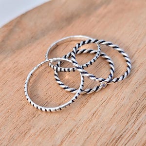 May include: A set of three silver-toned rings. One ring features a smooth, thin band with small etched markings, while the other two rings are crafted with a twisted, rope-like design. The metal has a polished finish with darkened accents.