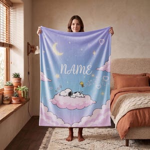 May include: A soft fleece blanket featuring a light blue and purple gradient background with a crescent moon, stars, and hearts. The text NAME is printed in white, with Snoopy sleeping on a pink cloud and Woodstock flying nearby.