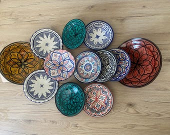 Op de afbeelding: Een verzameling van twaalf ronde keramische borden en kommen met ingewikkelde handgeschilderde geometrische en bloemmotieven in levendige kleuren, waaronder turkoois, mosterdgeel, terracotta, marineblauw en wit met geschulpte randen.