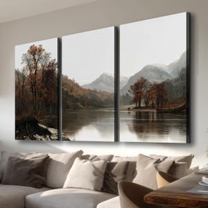 Peut inclure: Un ensemble de trois panneaux muraux représentant un paysage avec une rivière calme, des arbres aux couleurs automnales avec un feuillage orange et brun, et des montagnes enneigées au loin. La scène montre un petit bateau et deux silhouettes.