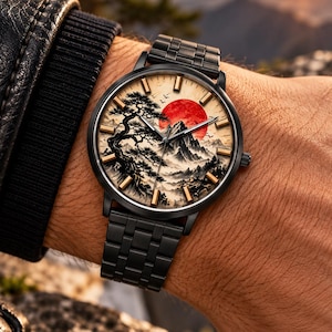 Peut inclure: Une montre-bracelet en métal noir avec un cadran rond illustré d'un paysage de montagne, d'un grand soleil rouge et d'un pin dans un style lavis. La montre possède des index dorés et un bracelet à maillons en métal noir.