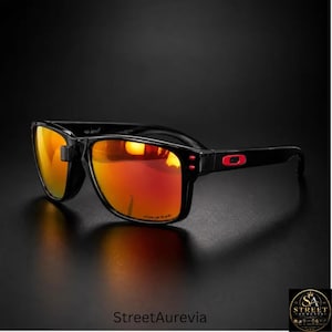 May include: Black sunglasses featuring rectangular frames and vibrant orange-red mirrored lenses. The temples display a prominent red rectangular logo accent near the hinges. The lenses are etched with the word Prizm in the lower corner.