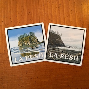 May include: Two square stickers featuring coastal landscape illustrations of La Push. The left sticker shows a rocky island with trees under a blue sky, while the right sticker depicts a dark cliffside by the ocean. Both have white borders and the text LA PUSH.