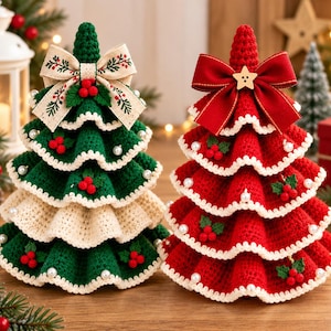 May include: Two tiered crochet Christmas trees, one green and one red, featuring ruffled layers with white trim, pearl accents, and small red berry clusters. The green tree has a beige bow with leaf patterns, while the red tree has a solid red bow.