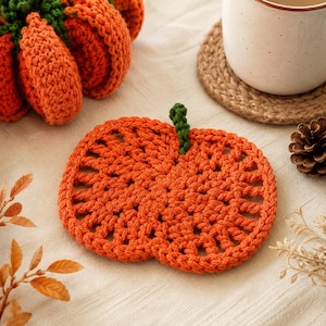 May include: A flat, orange, pumpkin-shaped crochet coaster featuring an openwork stitch pattern and a small green stem at the top. The coaster is crafted from yarn and displays a circular design with radiating segments, mimicking the appearance of a pumpkin.