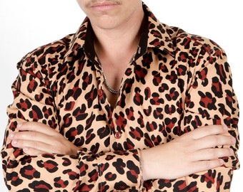 Pode incluir: Um homem vestindo uma camisa de botão de manga comprida com estampa de leopardo marrom, preto e vermelho. Ele está de pé com os braços cruzados na frente dele.