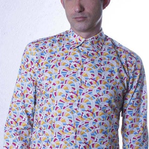 Puede incluir: Una camisa blanca de manga larga con botones y un estampado geométrico colorido. El estampado presenta un diseño repetitivo de círculos superpuestos en tonos de azul, amarillo, rosa y blanco.