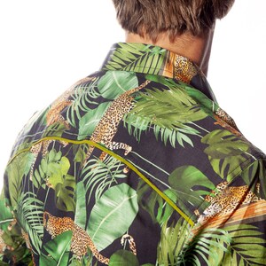 May include: A black button-down shirt with a tropical print featuring green leaves and leopard spots. The shirt has a yellow trim around the collar and down the front.